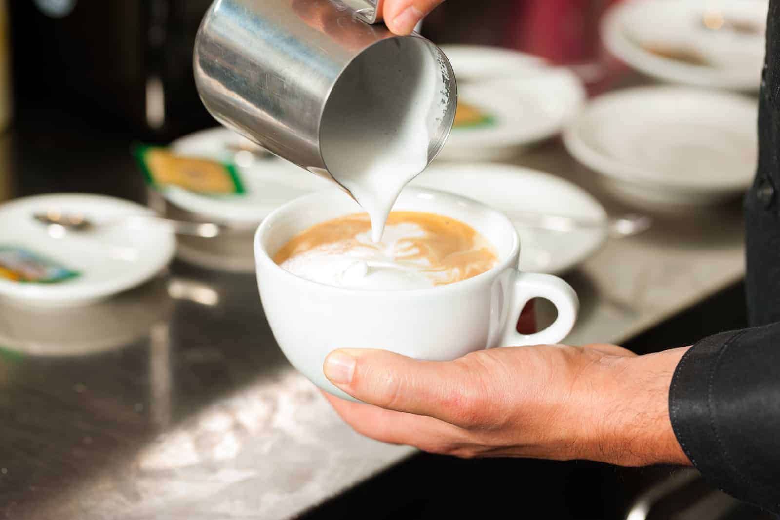 Barista making cappuccino in his coffeeshop or cafe, close-up