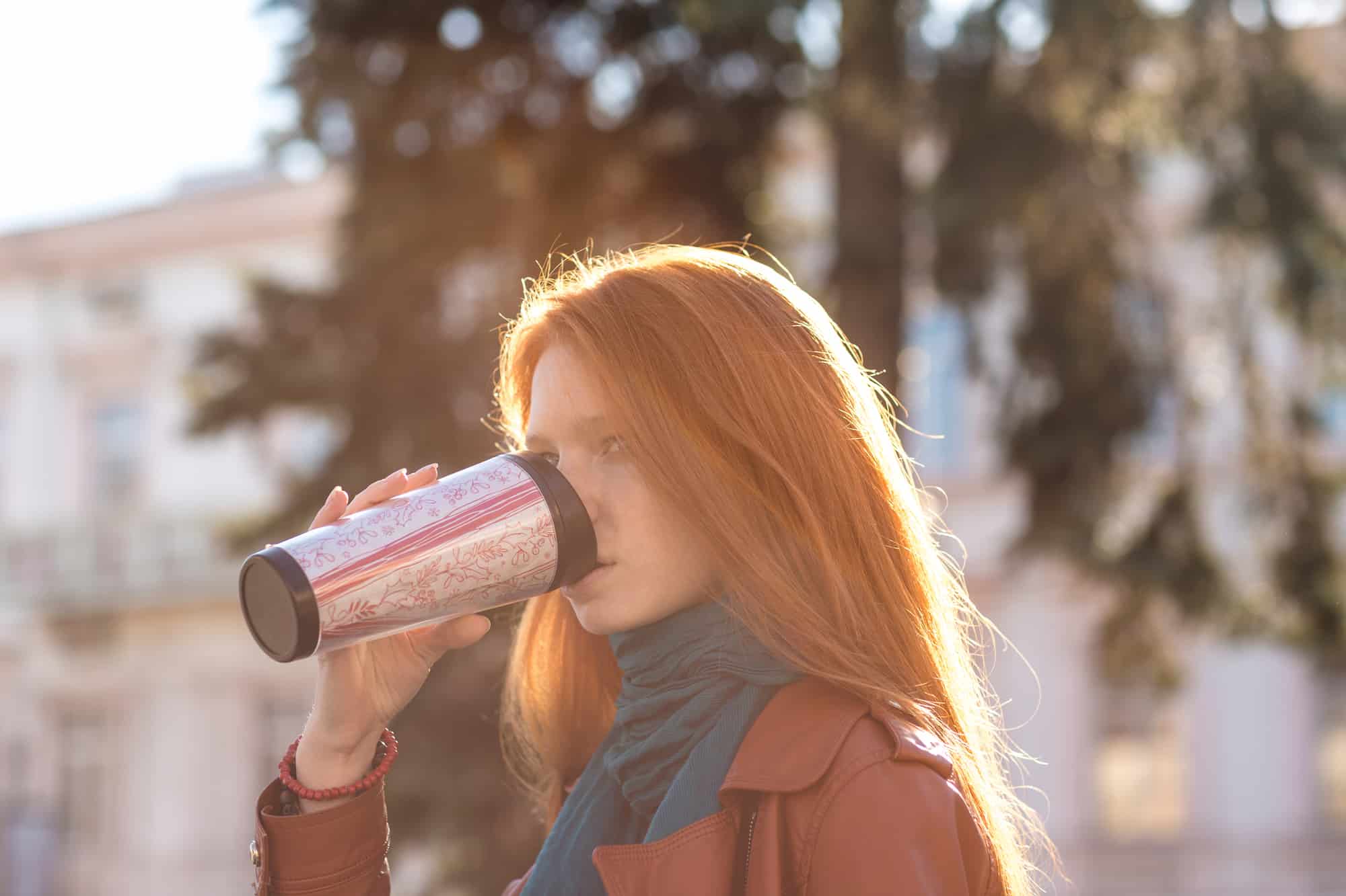 Beautiful redhead lady drinking coffee from tumbler