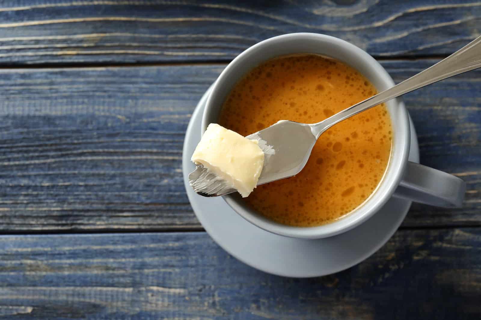 Cup of tasty butter coffee and shovel on wooden table